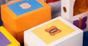 Home » Latest Printing News A close-up view of various colourful, custom-branded product boxes, including an orange box with a blue label and a white box.